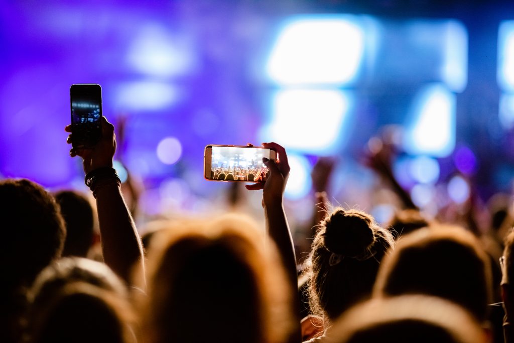Tangan penonton di konser mengangkat smartphone untuk merekam panggung, menggambarkan bagaimana konten buatan pengguna menjadi bagian penting dari strategi digital marketing.