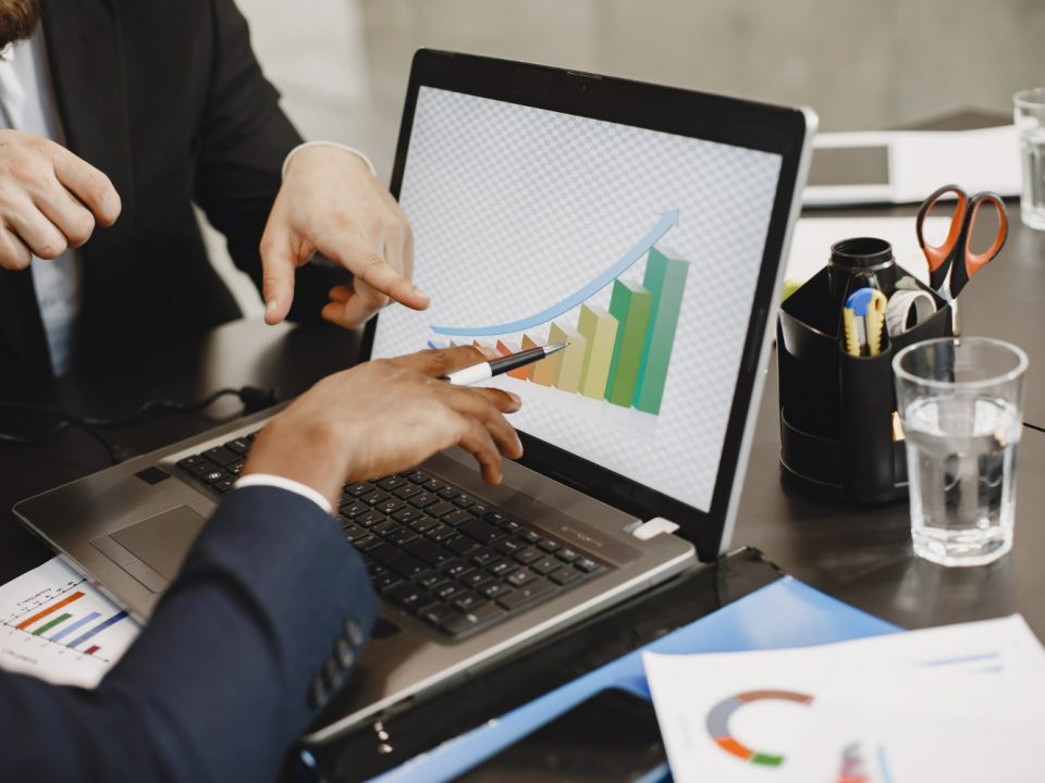 Dua pebisnis menganalisis grafik pertumbuhan di laptop, mendiskusikan angka dan strategi untuk mengukur ROI digital marketing.